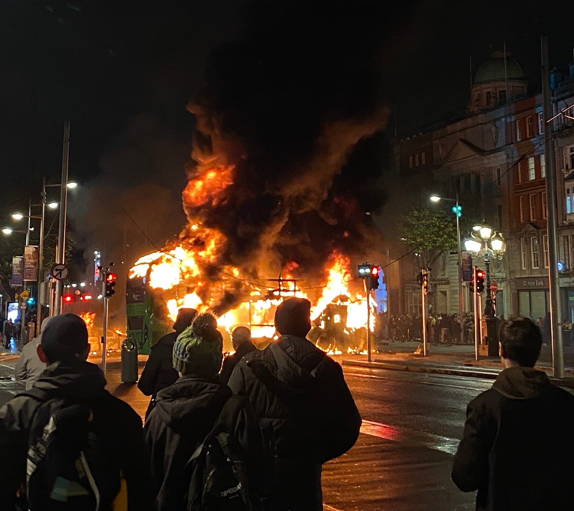 Onlookers watch a double-decker bus engulfed in flames on O'Connell Street, Dublin, at night.